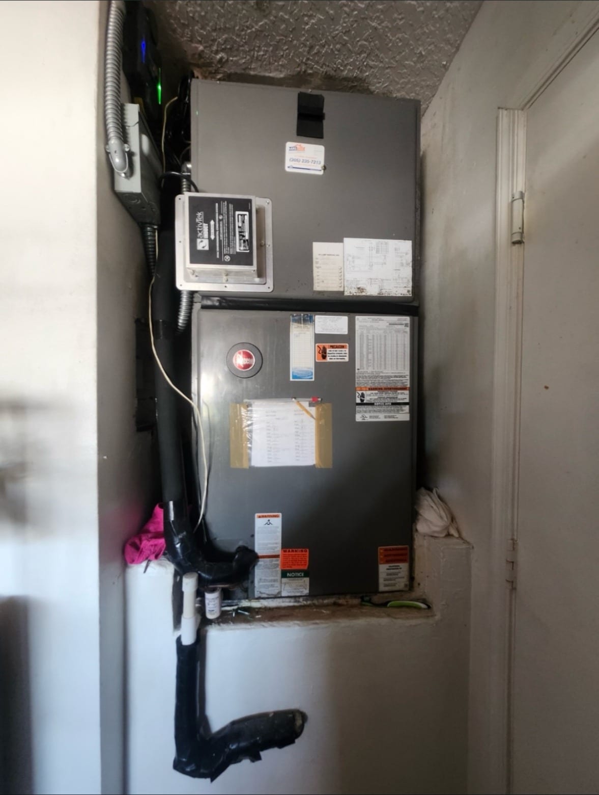 An air handler in a utility closet with its drain line and refrigerant lines in view
