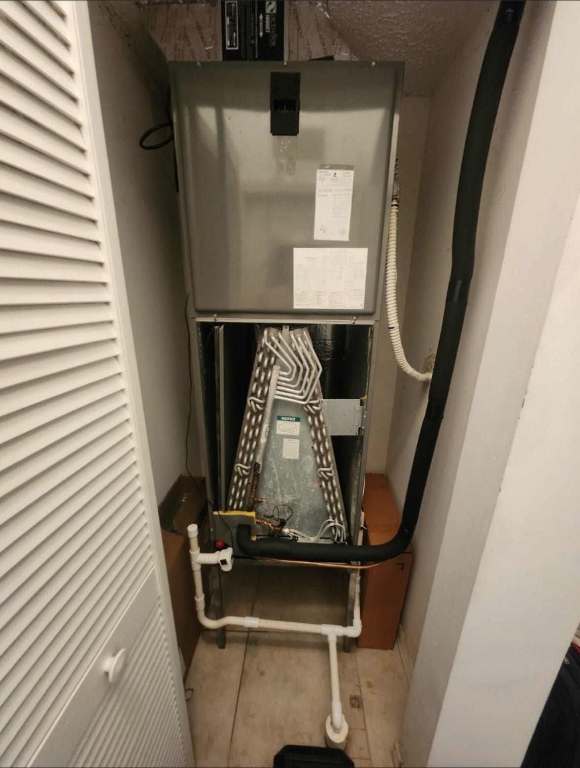 An air handler in a closet with its lower panel off and the coil showing