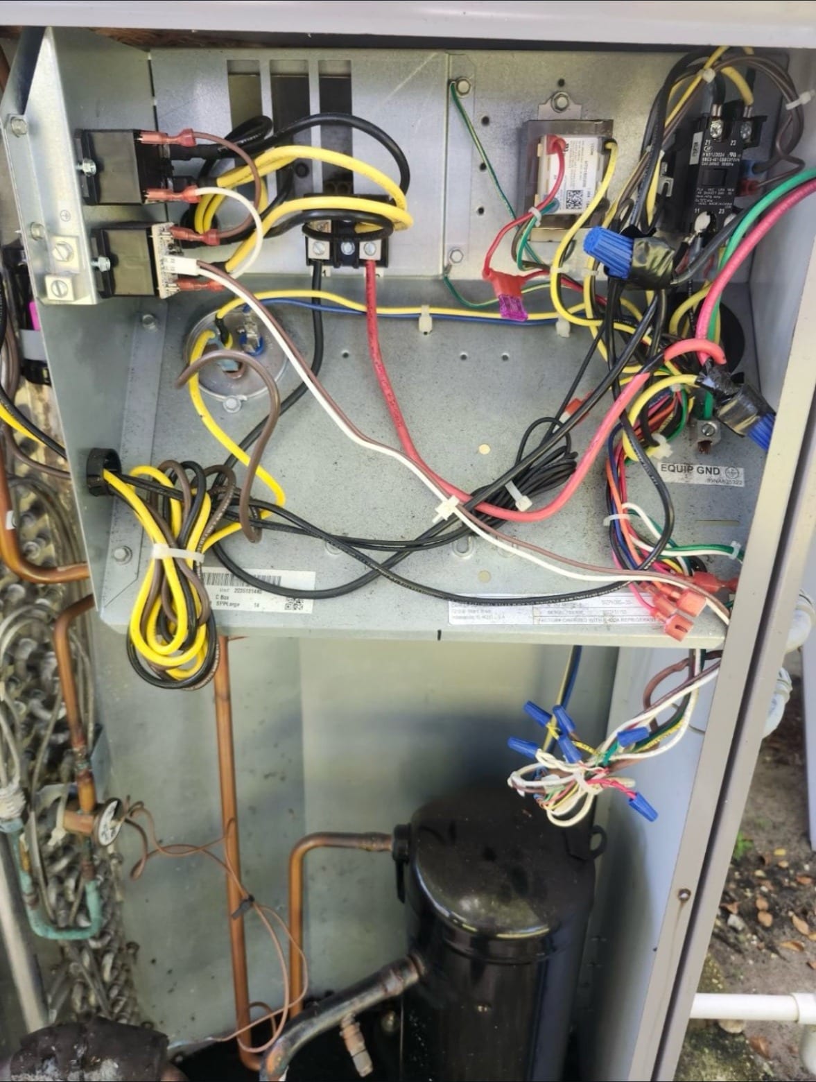 The open control panel of an outdoor AC unit, showing its wiring and capacitor