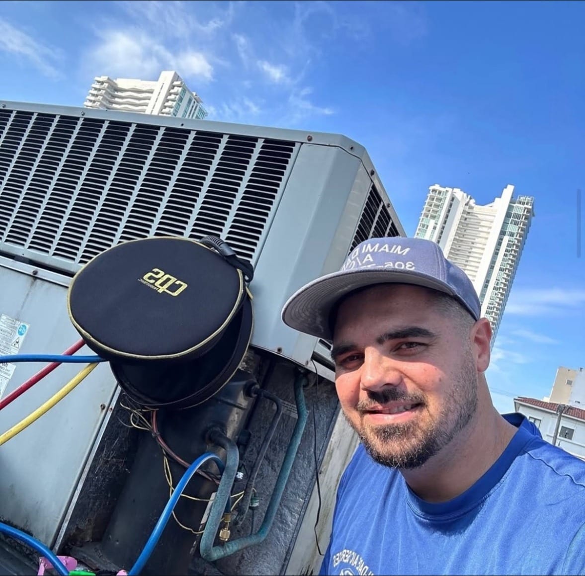 Joel Castillo smiling next to an open rooftop AC unit, with Miami towers behind him